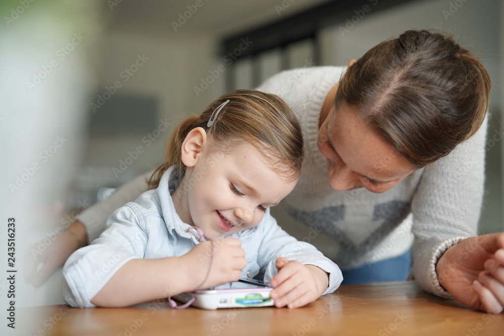 Mother and daughter having fun playing with child's tablet at home Mother and daughter having fun playing with child's tablet at home