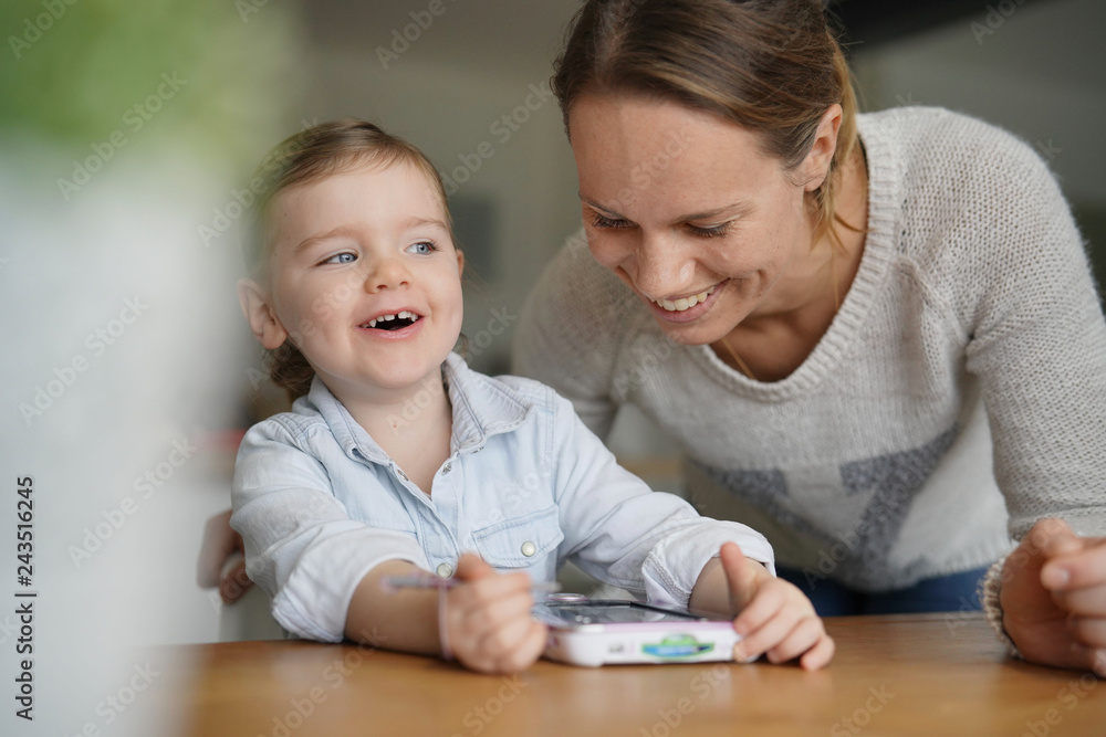 Mother and daughter having fun playing with child's tablet at home