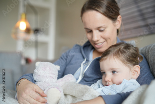 Mother comforting her young daughter on sofa at home