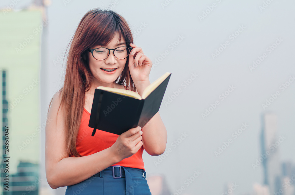 Smiling Young beautiful asian women in glasses reads book in summer city background Smiling Young beautiful asian women in glasses reads book in summer city background