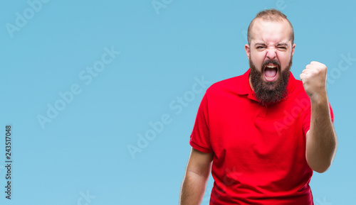 Young caucasian hipster man wearing red shirt over isolated background angry and mad raising fist frustrated and furious while shouting with anger. Rage and aggressive concept.