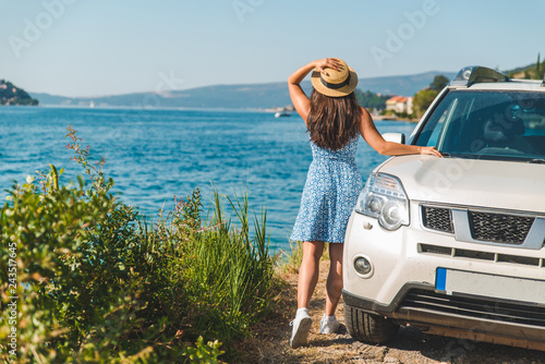 woman in blue dress standing near white car at seaside with beautiful view on bay and mountains