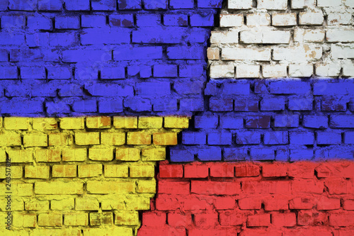 Flags of Ukraine and Russia on the brick wall with big crack in the middle. Symbol of problems between countries