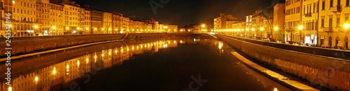 Panoramic View of the Illuminated buildings at night on the banks of the Arno river in Pisa and its reflection in the black waters.