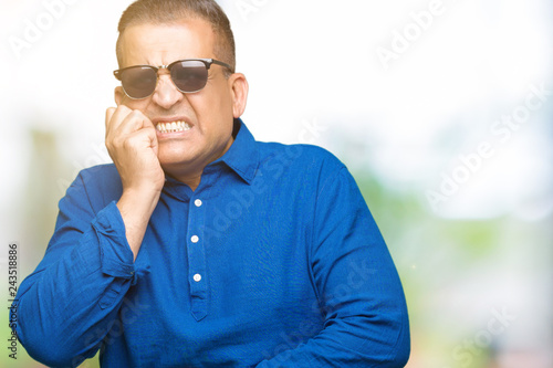 Middle age arab man wearing sunglasses over isolated background looking stressed and nervous with hands on mouth biting nails. Anxiety problem.