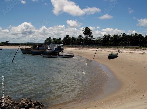 Boats and canoes on the beach. Blue sky with cloud. Palm trees.