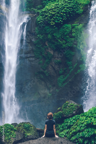 Young woman posing on a great Sekumpul waterfall in the deep rainforest of Bali island, Indonesia.