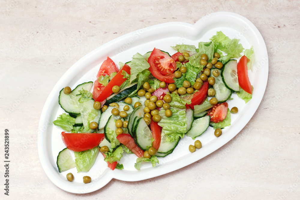 Original salad for healthy nutrition of cucumbers, tomatoes, lettuce and green peas on a white plate with olive oil, sprinkled with pepper on a marble table Original salad for healthy nutrition of cucumbers, tomatoes, lettuce and green peas on a white plate with olive oil, sprinkled with pepper on a marble table
