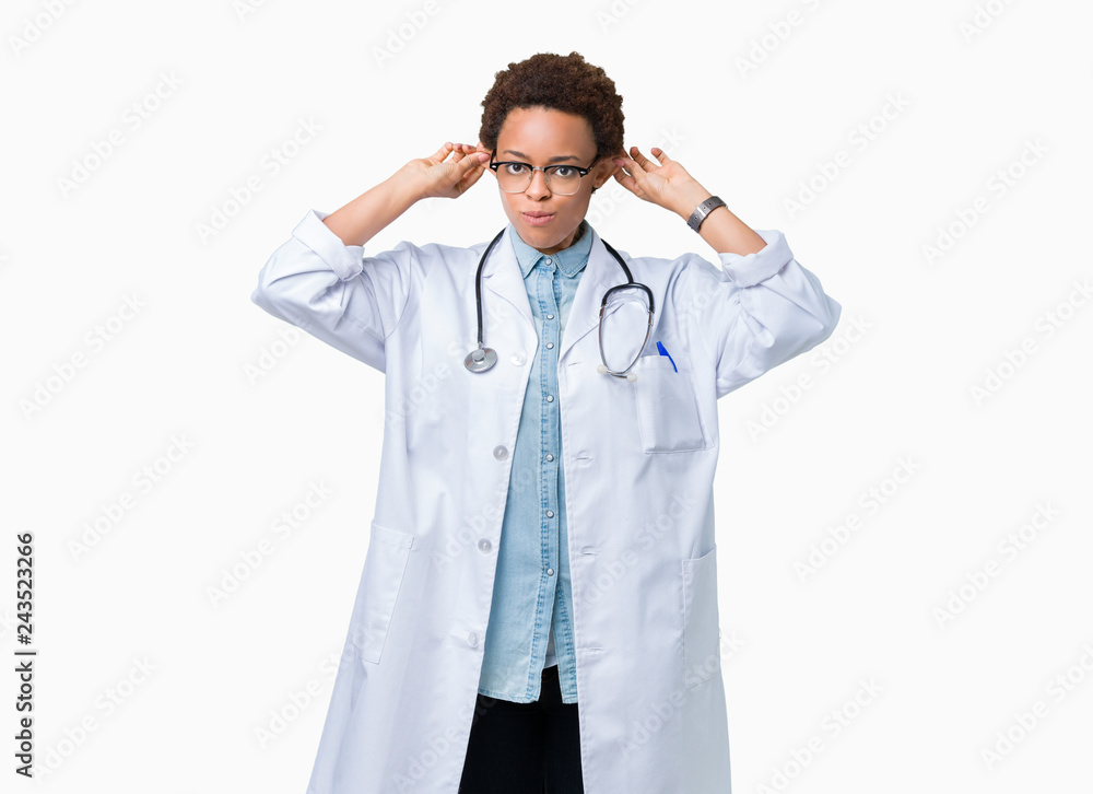 Young african american doctor woman wearing medical coat over isolated background Smiling pulling ears with fingers, funny gesture. Audition problem Young african american doctor woman wearing medical coat over isolated background Smiling pulling ears with fingers, funny gesture. Audition problem