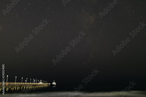 Fototapeta Naklejka Na Ścianę i Meble -  Night landscape. Small pleasure boat moored to a pier near the sea coast. Starry night sky over the sea.