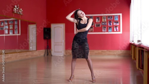 Beautiful slim flexible and sexy brunette in black tight suit doing streching exercises, touching her head and waist with hands and bending to the left /right. Light red accomondation photo