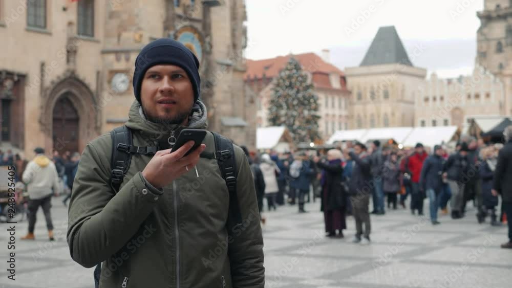 Handsome tourist young man use phone with voice recognition ai speech audio message smartphone on the christmas market. Cold winter in europe new year christmas Handsome tourist young man use phone with voice recognition ai speech audio message smartphone on the christmas market. Cold winter in europe new year christmas