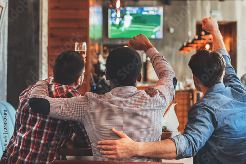 Three men watching football on TV in bar photo