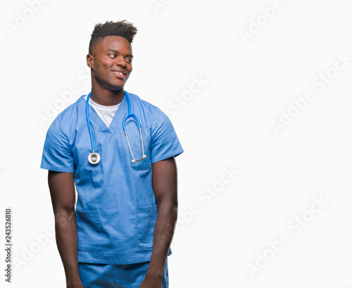 Young african american doctor man over isolated background wearing surgeon uniform looking away to side with smile on face, natural expression. Laughing confident.