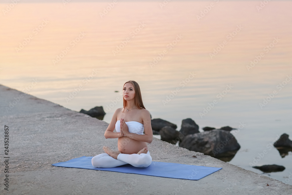 Beautiful pregnant woman doing yoga at the seaside