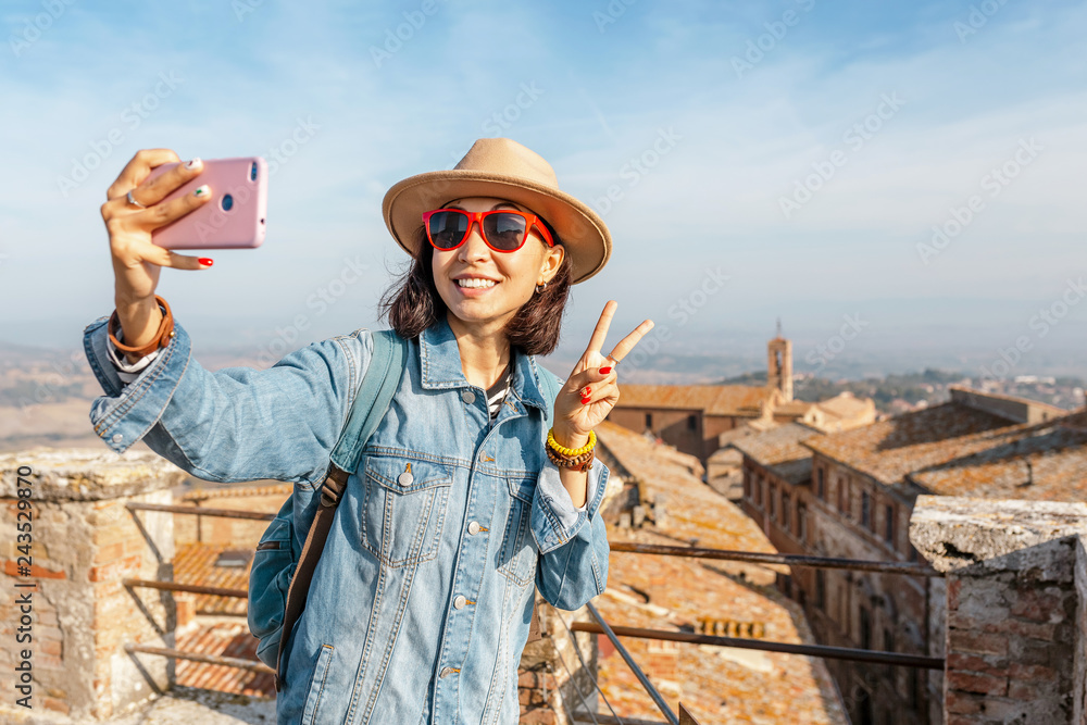 Happy asian tourist woman with smartphone in old town of Montepulciano, Tuscany. Vacation and travel in Italy concept