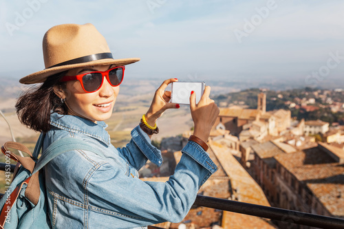 Happy asian tourist woman with smartphone in old town of Montepulciano, Tuscany. Vacation and travel in Italy concept