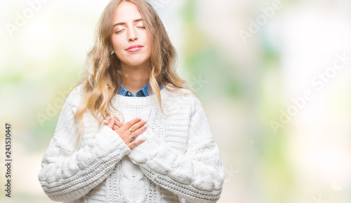 Beautiful young blonde woman wearing winter sweater over isolated background smiling with hands on chest with closed eyes and grateful gesture on face. Health concept.