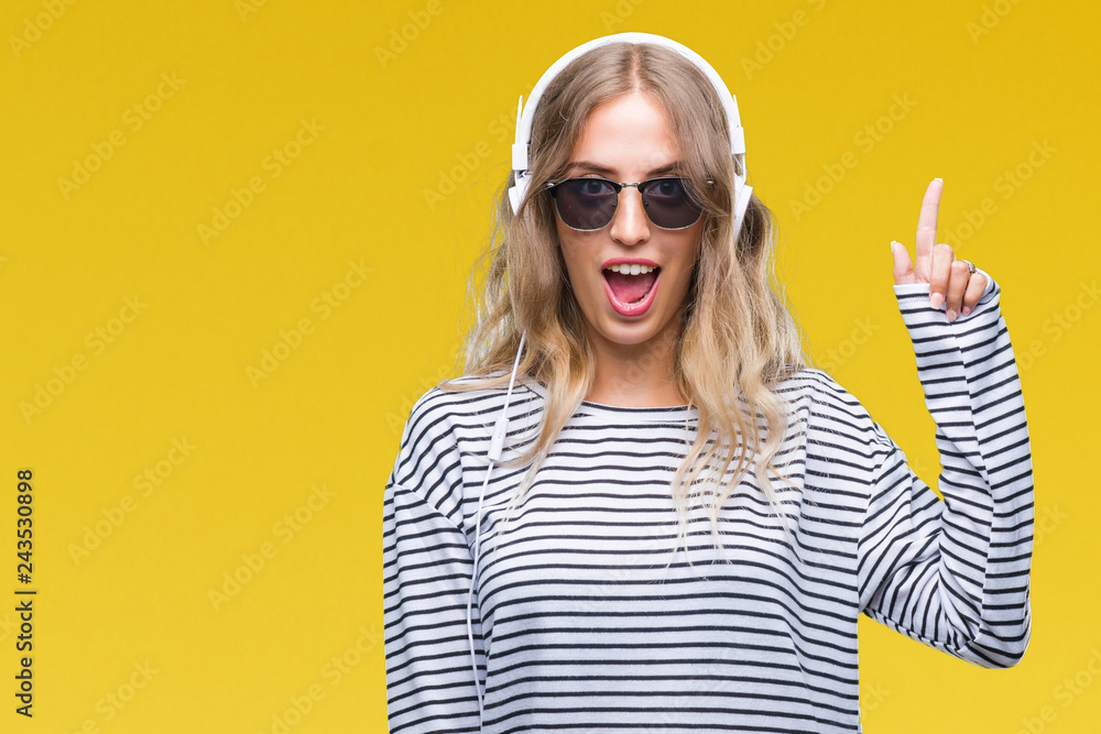 Beautiful young blonde woman wearing headphones and sunglasses over isolated background pointing finger up with successful idea. Exited and happy. Number one. Beautiful young blonde woman wearing headphones and sunglasses over isolated background pointing finger up with successful idea. Exited and happy. Number one.