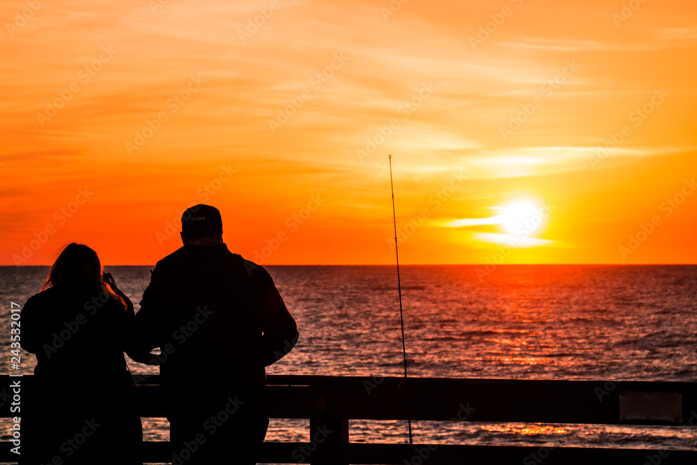 silhouette of man sitting on pier at sunset