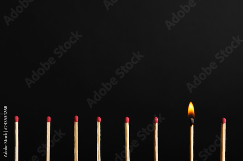 Row of matchsticks with burning one on black background. Be different