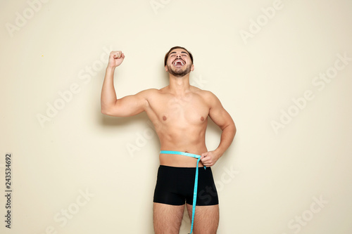 Fit man measuring his waist on color background. Weight loss