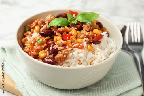 Tasty chili con carne served with rice in bowl on table