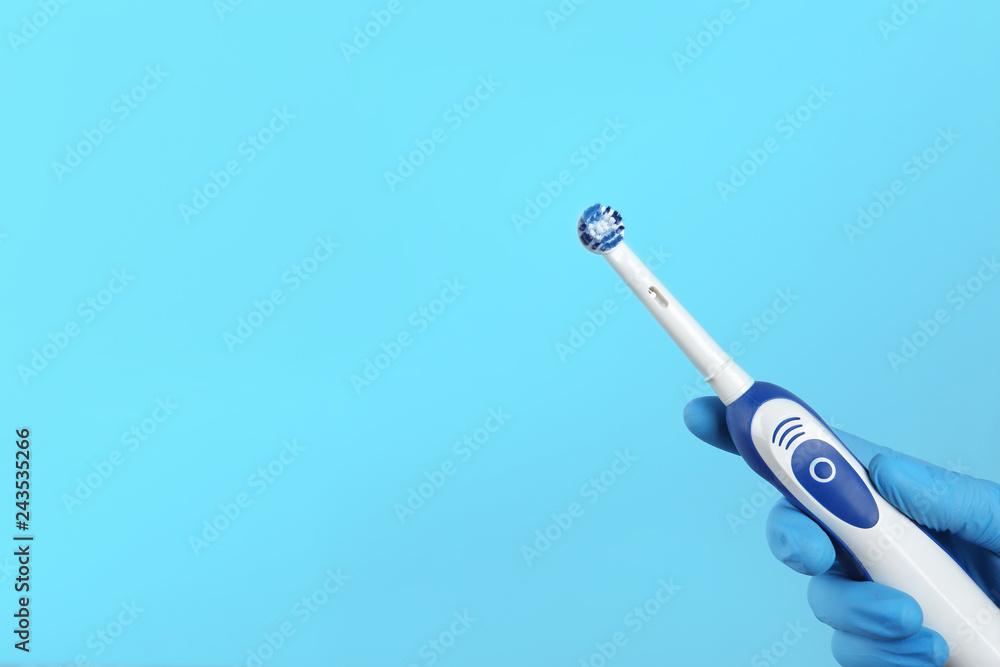 Dentist holding electric toothbrush on color background, space for text Dentist holding electric toothbrush on color background, space for text