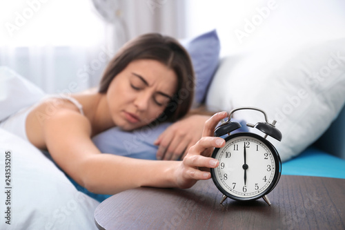 Young woman turning off alarm clock in morning. Bedtime