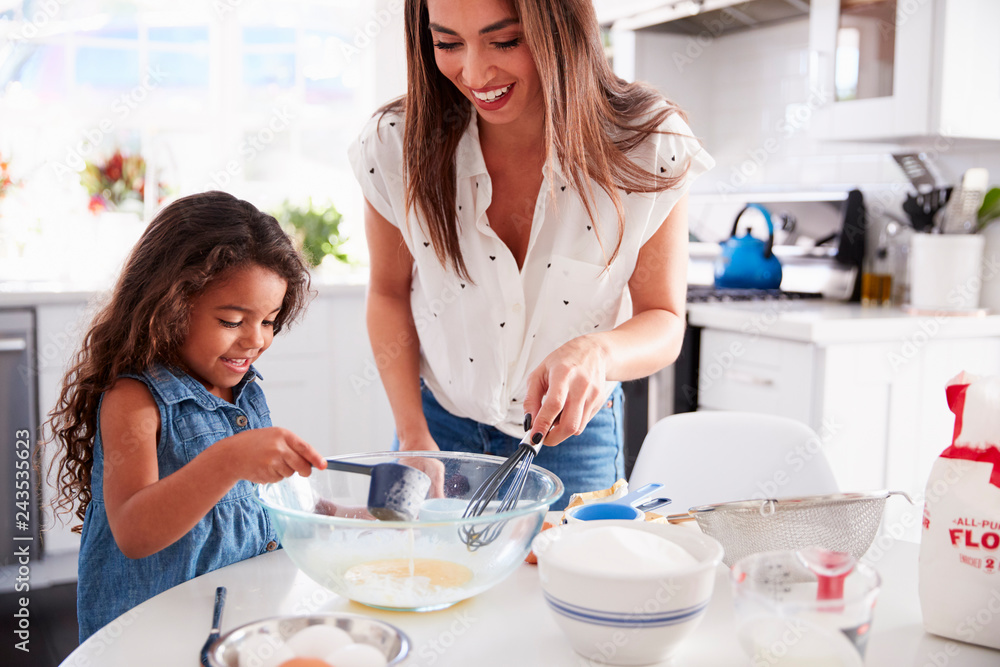 Young Hispanic girl making cake in the kitchen with her mum, waist up