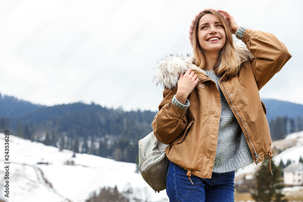 Young woman in warm clothes near snowy hill, space for text. Winter vacation Young woman in warm clothes near snowy hill, space for text. Winter vacation