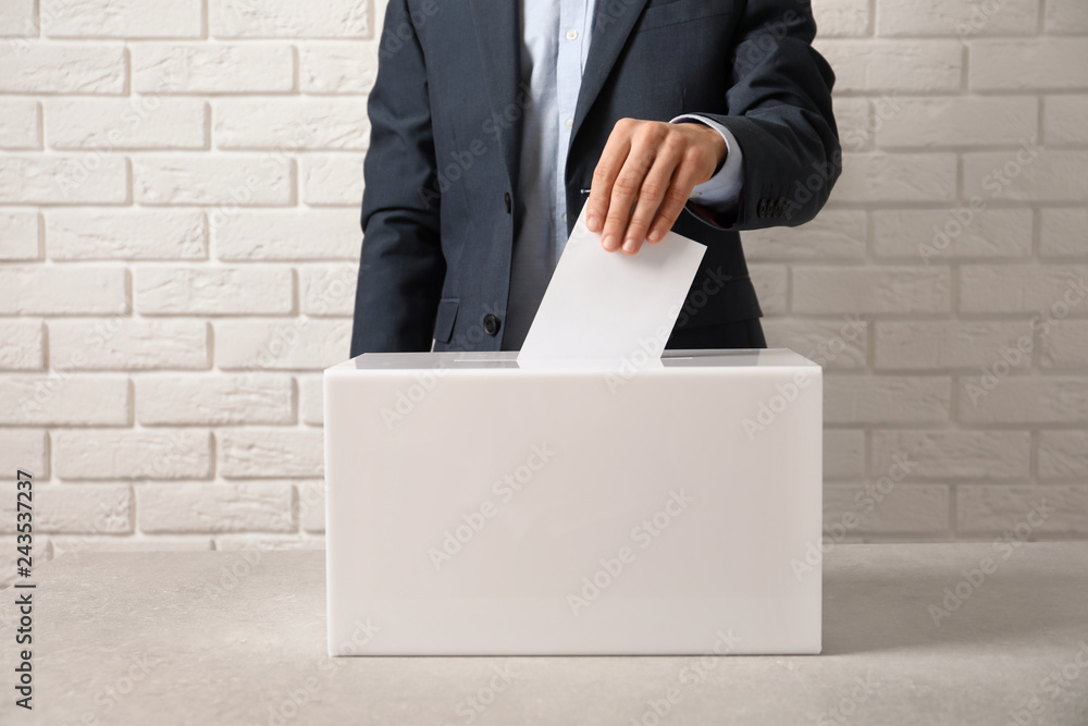 Man putting his vote into ballot box on table against brick wall, closeup Man putting his vote into ballot box on table against brick wall, closeup