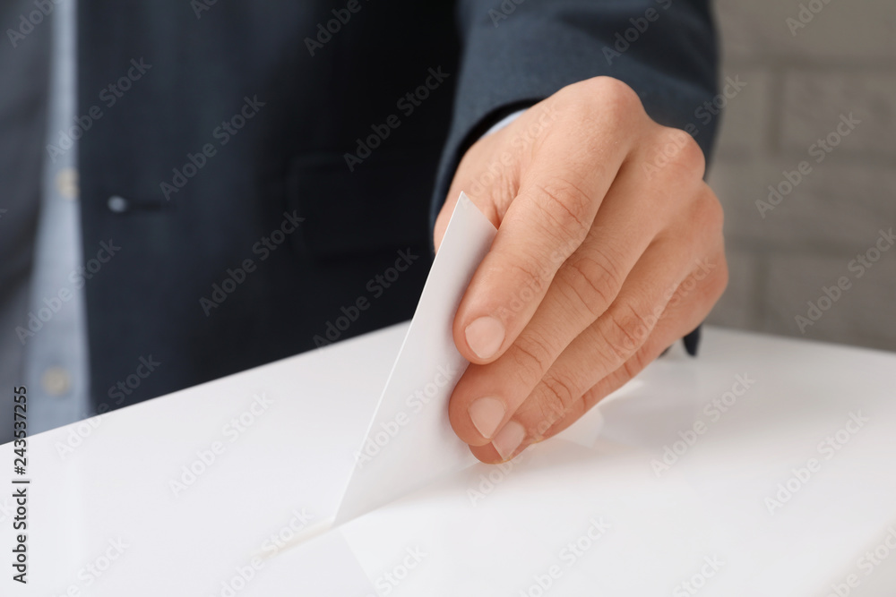 Man putting his vote into ballot box against brick wall, closeup Man putting his vote into ballot box against brick wall, closeup