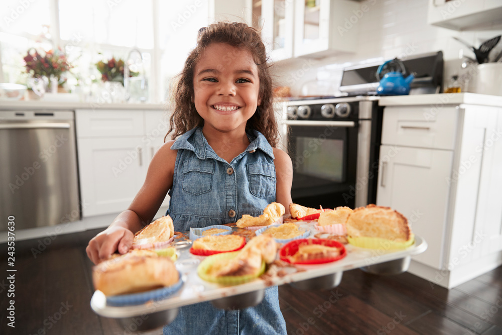 Young Hispanic girl standing in kitchen presenting cakes sheÕs baked and smiling to camera
