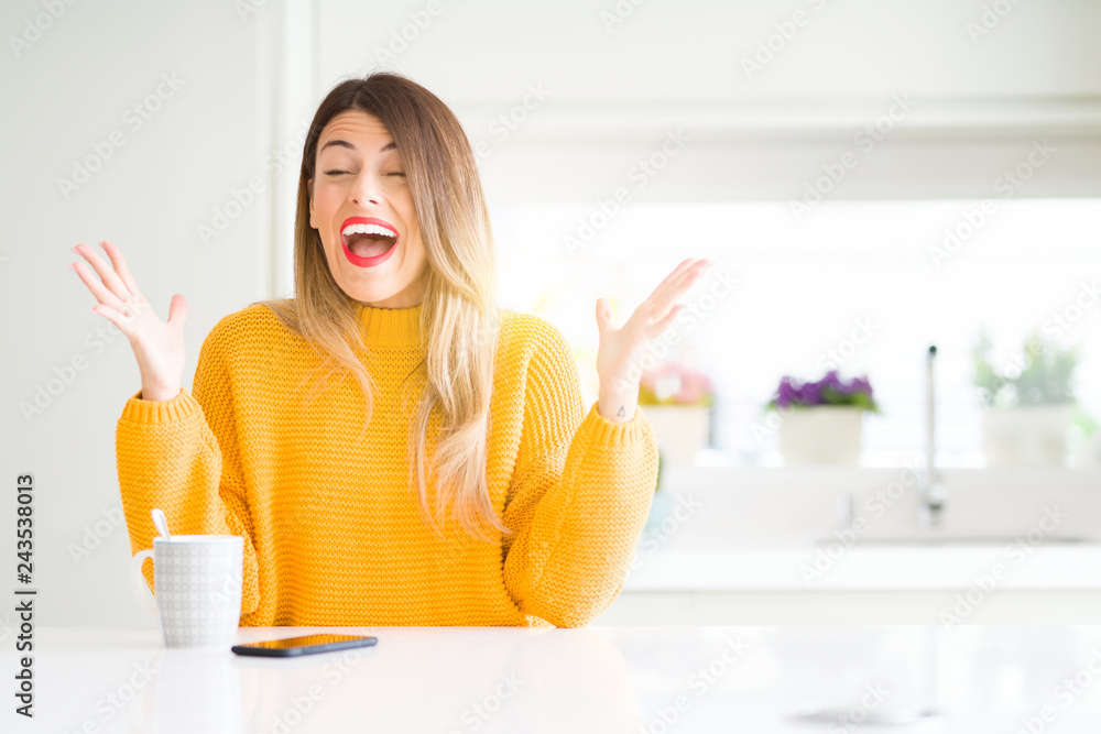 Young beautiful woman drinking a cup of coffee at home celebrating mad and crazy for success with arms raised and closed eyes screaming excited. Winner concept Young beautiful woman drinking a cup of coffee at home celebrating mad and crazy for success with arms raised and closed eyes screaming excited. Winner concept