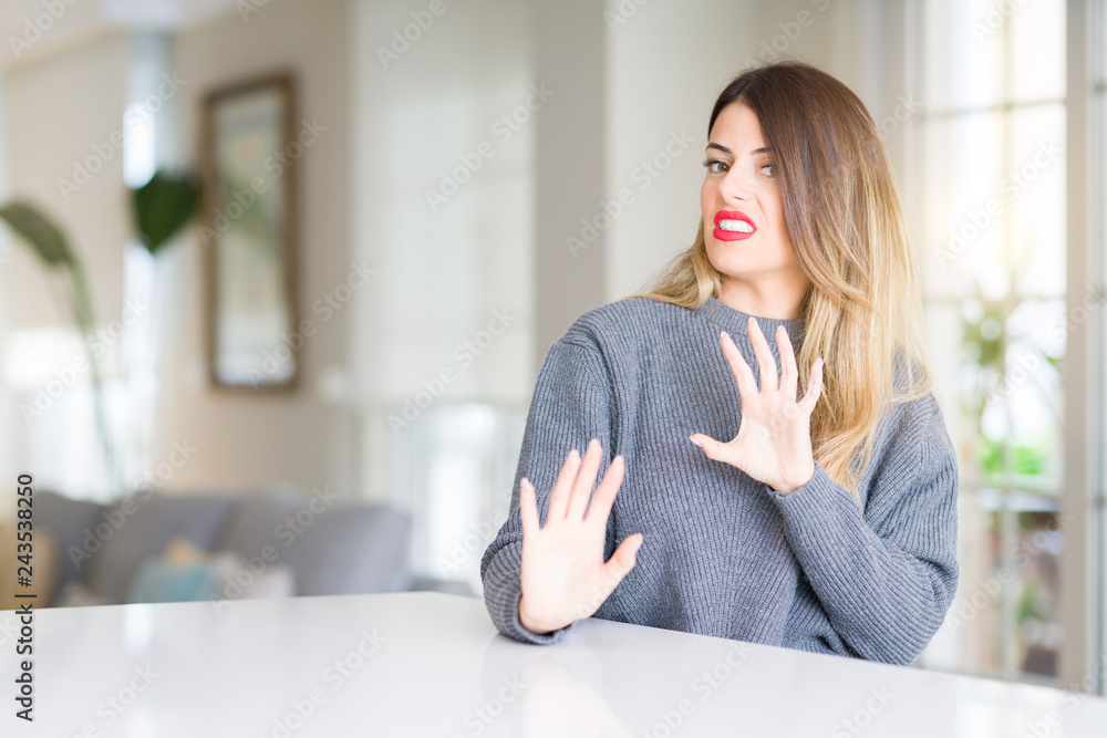 Young beautiful woman wearing winter sweater at home disgusted expression, displeased and fearful doing disgust face because aversion reaction. With hands raised. Annoying concept. Young beautiful woman wearing winter sweater at home disgusted expression, displeased and fearful doing disgust face because aversion reaction. With hands raised. Annoying concept.