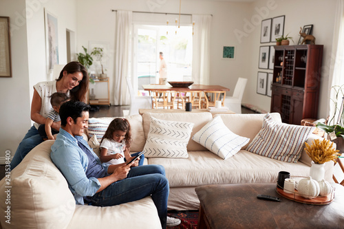 Young Hispanic family sitting on sofa reading a book together in their living room