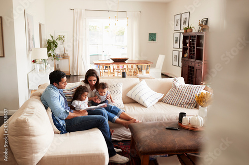 Valokuva Young Hispanic family sitting on sofa reading a book together in the living room