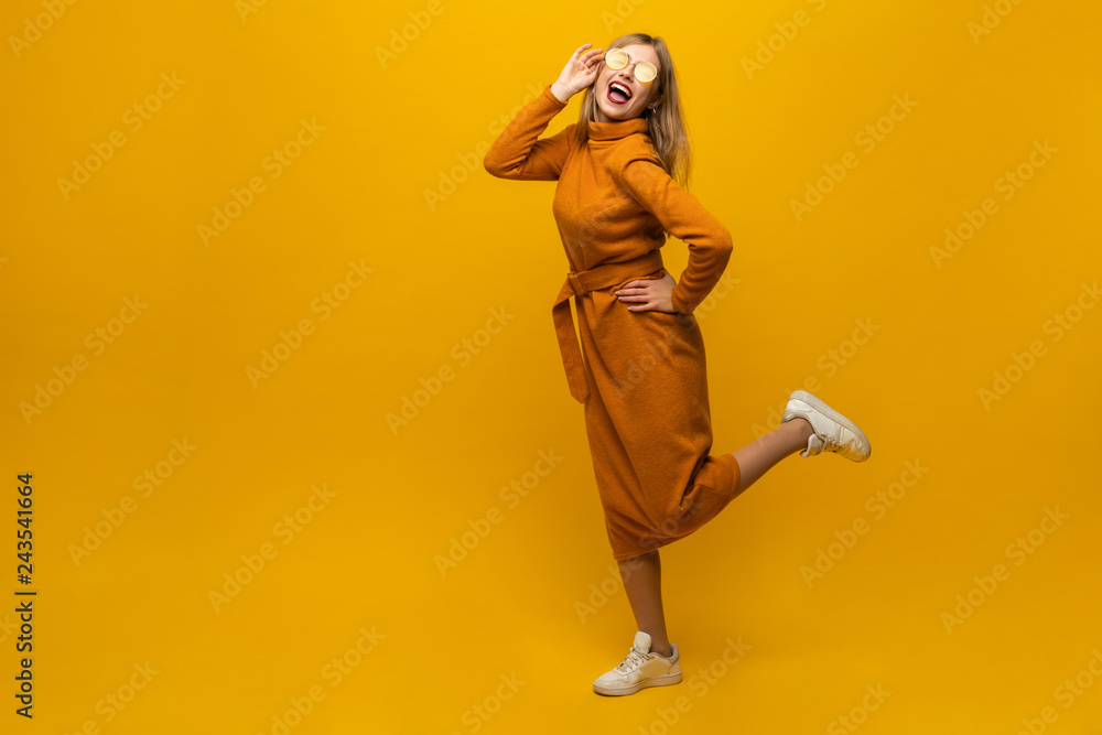 Full length portrait of a cheerful beautiful girl wearing dress having fun and dancing isolated over yellow background. Full length portrait of a cheerful beautiful girl wearing dress having fun and dancing isolated over yellow background.