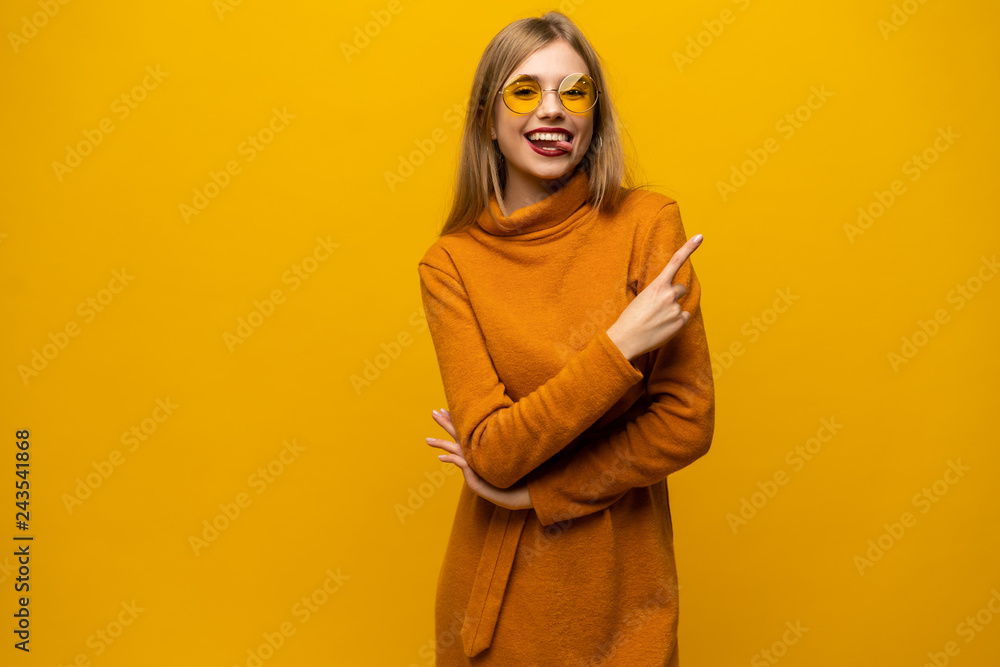 Cheerful lovely young woman standing and pointing away over yellow background. Cheerful lovely young woman standing and pointing away over yellow background.