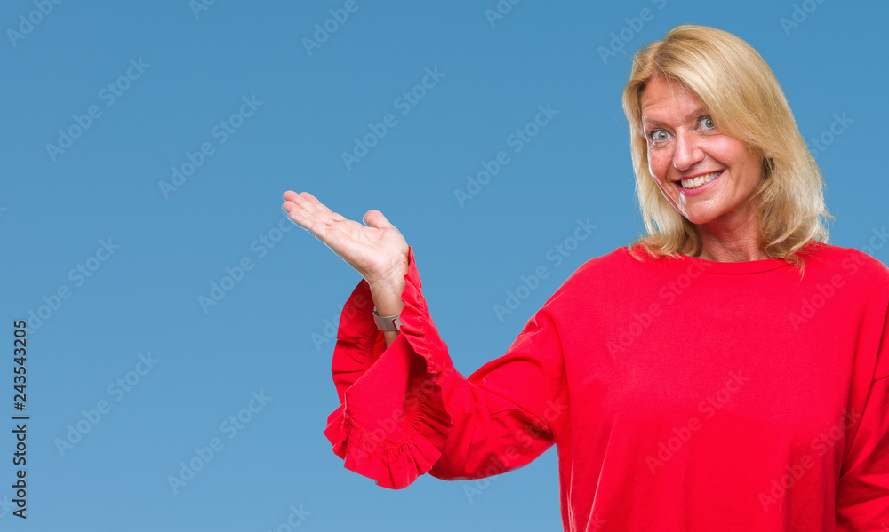 Middle age blonde woman over isolated background smiling cheerful presenting and pointing with palm of hand looking at the camera. Middle age blonde woman over isolated background smiling cheerful presenting and pointing with palm of hand looking at the camera.