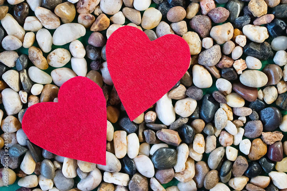 Two red decorative hearts and gray sea pebbles. Valentine's Day Concept. Two red decorative hearts and gray sea pebbles. Valentine's Day Concept.
