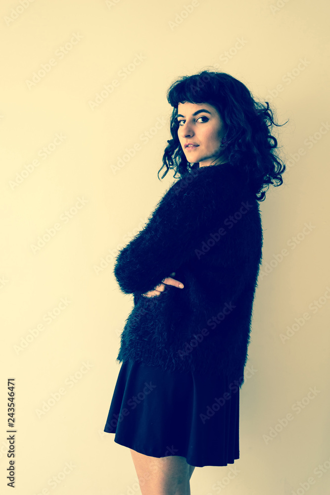 Fototapeta premium Portrait of a beautiful serious young woman in an elegant dress while standing in front of a white wall.
