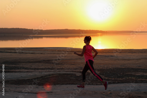 Young beautiful woman is running along the seashore on the orange sunset background