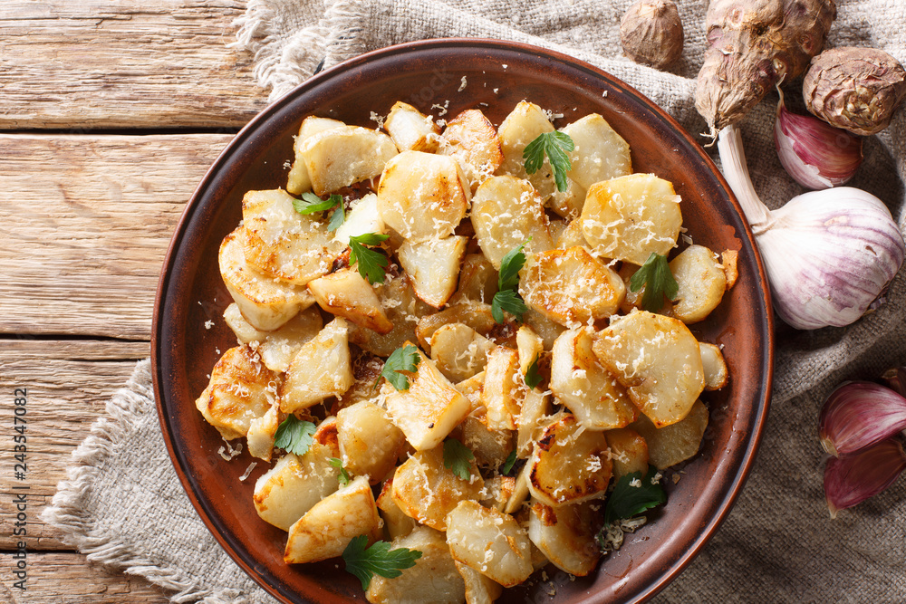 Spicy fried Jerusalem artichoke with garlic, cheese and parsley closeup on a plate. horizontal top view Spicy fried Jerusalem artichoke with garlic, cheese and parsley closeup on a plate. horizontal top view