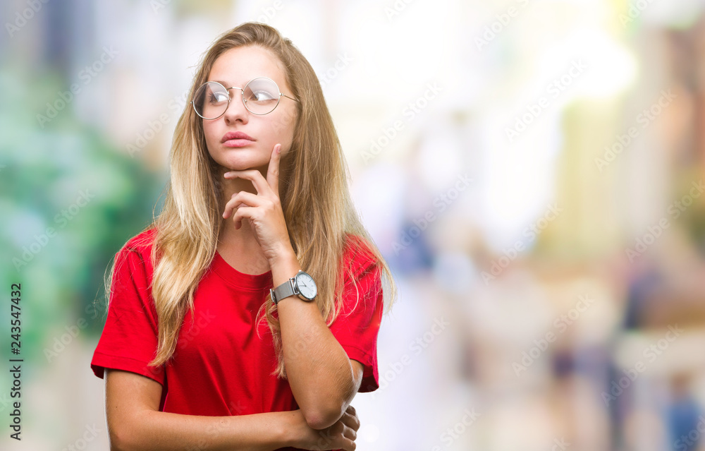 Young beautiful blonde woman wearing glasses over isolated background with hand on chin thinking about question, pensive expression. Smiling with thoughtful face. Doubt concept.