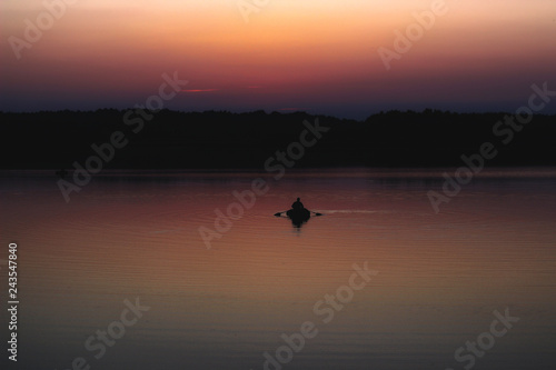 Silhouette of a man which floating on a boat on the sea at sunset time. © volhavasilevich