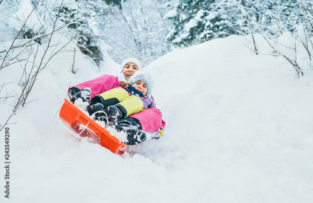 Mother with daughter slide down from snow slope together sitting in one slide.Winter activities concept image.