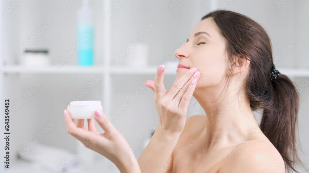 Young woman smiling and enjoying applying anti-ageing moisturizing cream on perfect skin face Young woman smiling and enjoying applying anti-ageing moisturizing cream on perfect skin face