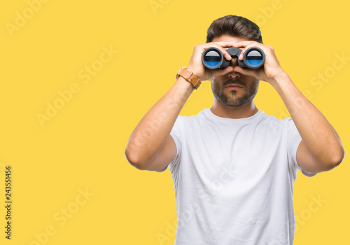 Young handsome man looking through binoculars over isolated background with a confident expression on smart face thinking serious